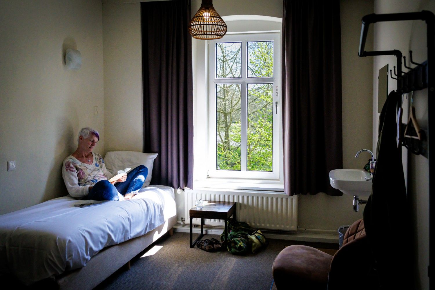 Deelnemer leest een boek in een lichte kamer van het Dominicanenklooster Huissen, met uitzicht op de groene tuin vanuit het raam.