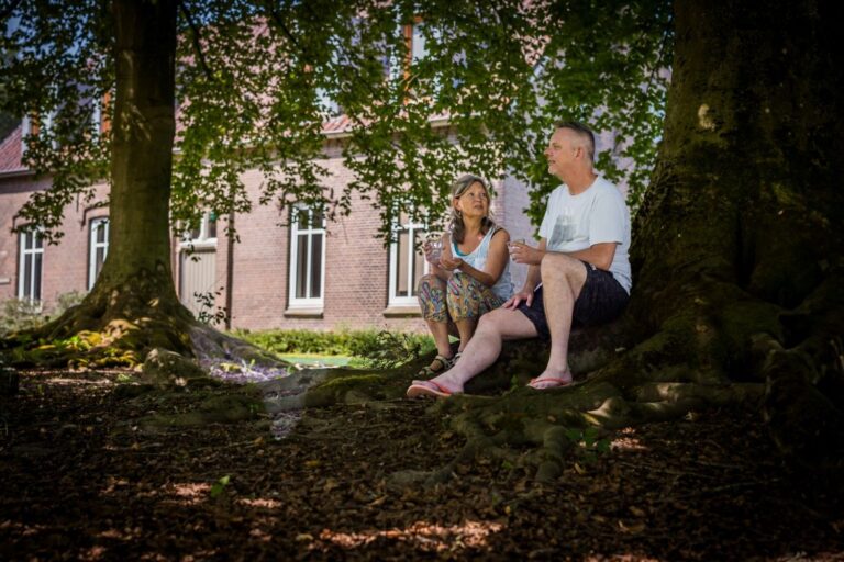 Deelnemers spreken over verbinding en leiderschap onder een boom in de tuin van het Dominicanenklooster Huissen, omringd door rust en natuur.