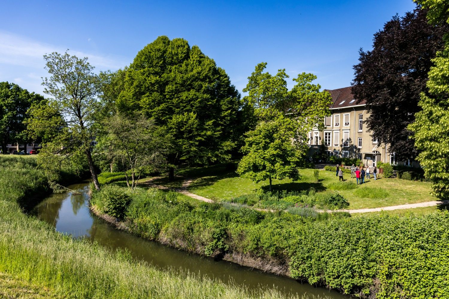 Groene kloostertuin van het Dominicanenklooster Huissen met deelnemers die wandelen langs het water op een zonnige dag.